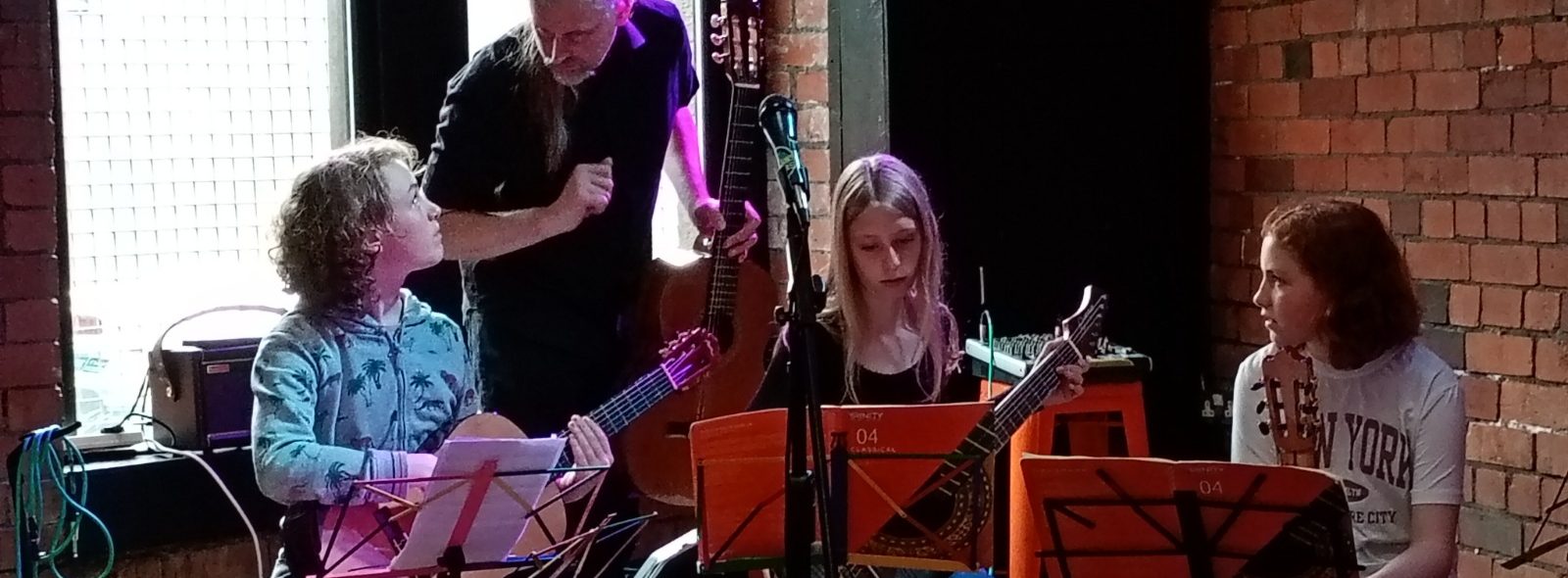 Guitar teacher guides a small group of young classical guitarists prepare to perform on stage.